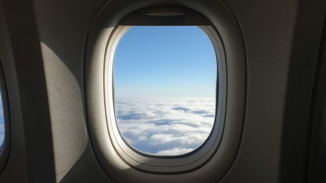 Stunning view of fluffy white clouds and blue sky seen through an airplane window. Ideal for travel and tourism concepts.