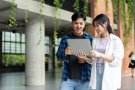 Young Asian students review a laptop together in a modern university environment, showing peer collaboration, digital education, startup preparation, freelance planning, and teamwork.