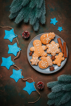 Christmas gingerbread cookies in a plate, garland of blue wooden stars and fir branches on dark grunge background, top view, flat lay