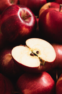 Close-up of ripe red apple cut in half with seeds on whole fruits backdrop. Macro vertical texture of fresh organic gala apple for autumn harvest background, healthy diet and food styling design.