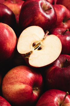 Red apples background texture with one cut slice showing core and seeds. Fresh ripe organic fruits close up top view. Healthy sweet vegan food backdrop for harvest and autumn season.