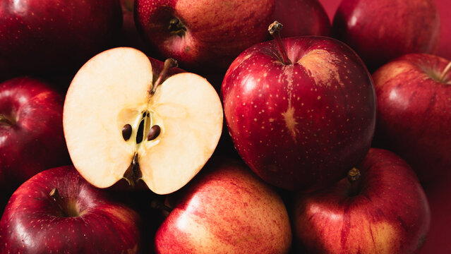 Horizontal background of ripe red apples with one sliced half showing core and seeds. Close-up overhead view of fresh organic fruits texture. Healthy sweet vegan food backdrop for harvest.