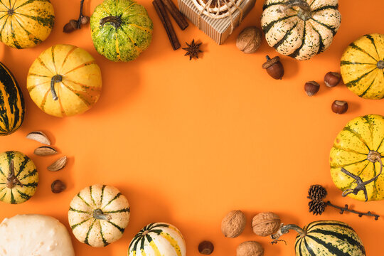 Autumn harvest mockup with decorative pumpkins, nuts, spices and gift box forming a frame on orange background. Flat lay top view thanksgiving day border template with copy space for text.