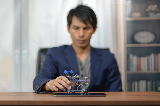 Young Man Sitting at Desk with Miniature Shopping Cart Model in Office