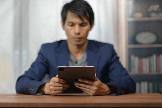 Man Using Tablet Computer at Desk in Office with Bookshelf in Background