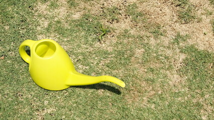 Bright yellow watering can sits on a dry patchy grass lawn © aziseptian