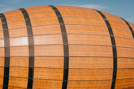 curved wooden exterior cladding with vertical dark metal bands on modern building under blue sky, warm light