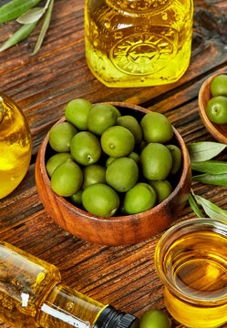 Green olives, olive oil bottles and wooden bowl rustic composition