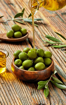 Pouring olive oil over fresh green olives in wooden bowl