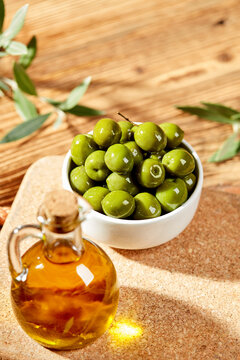 Green olives and olive oil arranged on cork board