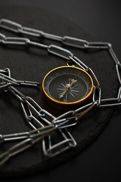 Compass Enclosed by Metal Chain on Dark Surface: Navigation and Restriction Concept