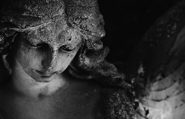 Fototapeta premium Sad angel statue with bowed head, symbolizing grief, compassion, loneliness, loss and eternal remembrance.
