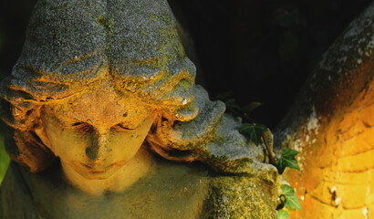 Fototapeta premium Weathered angel statue in warm sunlight, symbolizing grief, compassion, remembrance and hope.