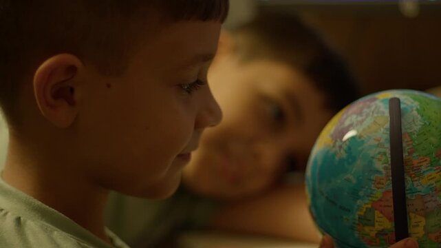 Young boy gazes at globe with wonder. Friend leans close, smiling softly. Warm light bathes their curious faces. Perfect for travel, education, or childhood themes