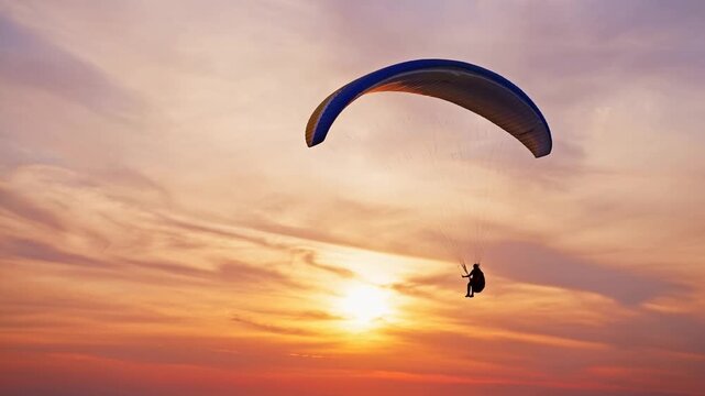 Tracking aerial pan of paraglider pilot gliding across sunset sky over coastal horizon