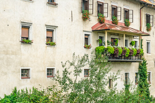Old European building facade with balcony, windows, and blooming flowers in window boxes