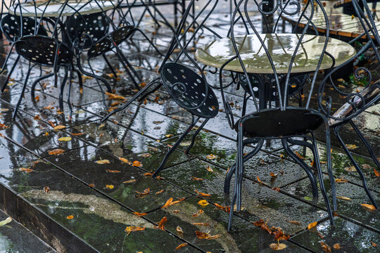 Empty cafe terrace with wrought iron tables and chairs in the rain with fallen autumn leaves