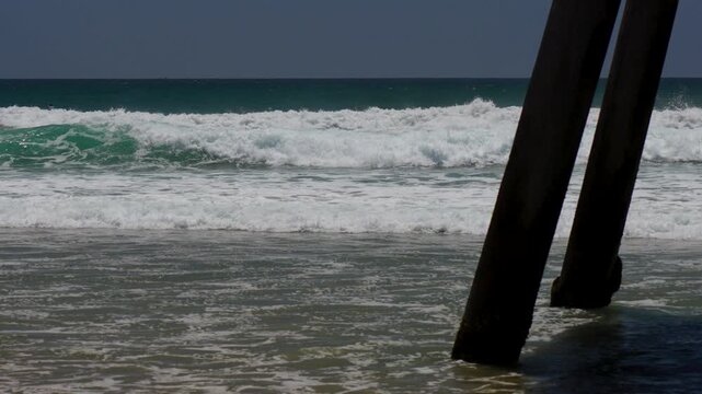 slow motion waves breaking next to pylons of a beach pier