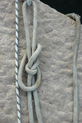 Close up view of a thick grey marine rope tied into a figure eight loop knot resting against a rough stone pie surface outdoors. © nahhan