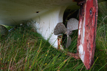 A metal propeller and weathered red rudder beneath a boat hull on Lewis and Harris, Outer Hebrides, Scotland. © George
