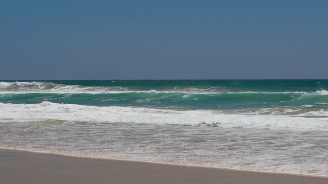 Wide shot of waves breaking in the ocean and on the sand