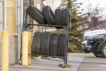 Stack of new tires on metal rack beside garage entrance © primestockphotograpy