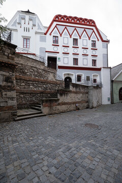 A picturesque historic building featuring unique red ornamental trim stands along a quiet cobblestone street in Cesky Krumlov.