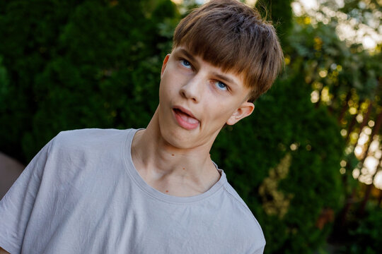Cheeky teenage boy sticking out tongue and making funny face with head tilted, wearing a gray shirt in a green garden, humor and fun concept portrait, grainy film texture, high quality photo