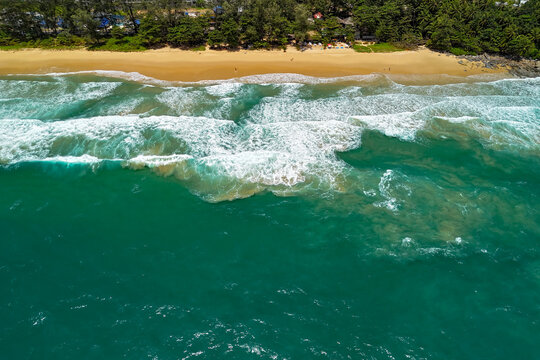Picturesque tropical coastline featuring buildings amidst jungle vegetation and a golden sand beach with heavy surf and dangerous rip currents, swimming is prohibited.