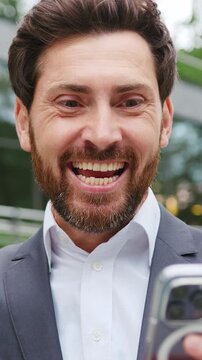 Close-up of a smiling man holding a smartphone and checking email outdoors, expressing happiness and positive emotions while reading a message on a mobile device. Slow motion