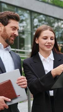 Professional man and woman using a tablet and having a business discussion outdoors, representing remote work, teamwork, digital communication, and modern mobile office lifestyle.