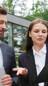 Professional business colleagues discussing a project and reviewing information on a digital tablet outdoors. Corporate teamwork, business communication, collaboration, planning, remote work, and