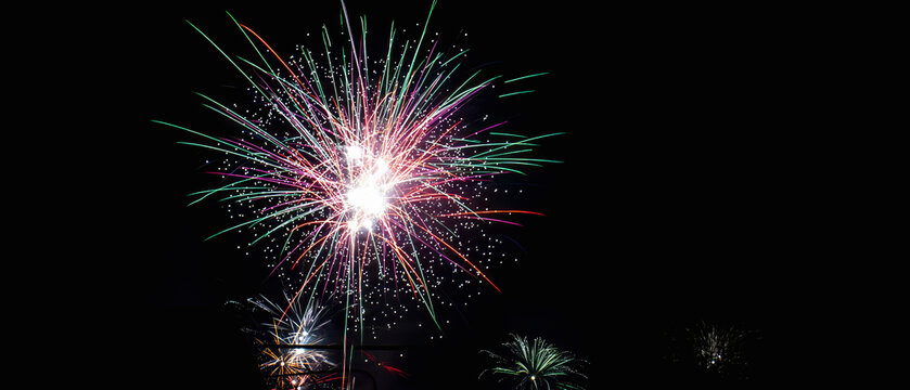 Colorful fireworks bursting in a dark night sky with pink, purple, green, red and white light trails, festive celebration display with copy space