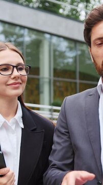 Portrait of businessman and businesswoman standing outdoors, looking at a laptop screen and having a business conversation. Professional colleagues discussing work, technology, teamwork, and business