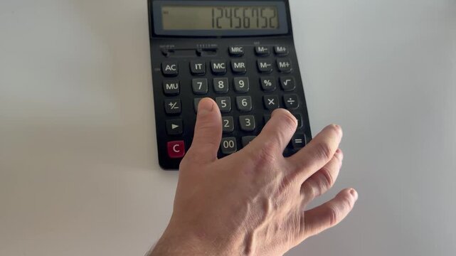 Hand using a black calculator for numerical calculations, financial planning activity, accounting task, data analysis process.