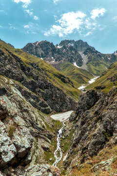 Rocky alpine valley with a cascading stream, lingering snowfields and rugged peaks near Badak Lake in Uzbekistan.