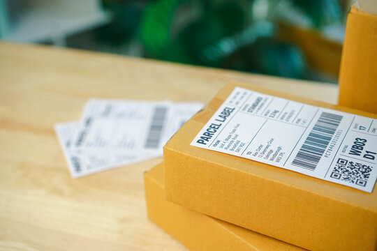 delivering,Cardboard parcels with shipping labels and barcodes sit stacked on a table. Close-up of QR codes and delivery details illustrates logistics, online order fulfillment, and shipment tracking.