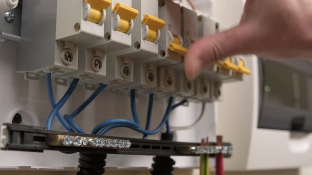 Person turns on electricity in house, hand clicks electric circuit breakers in electrical panel close-up