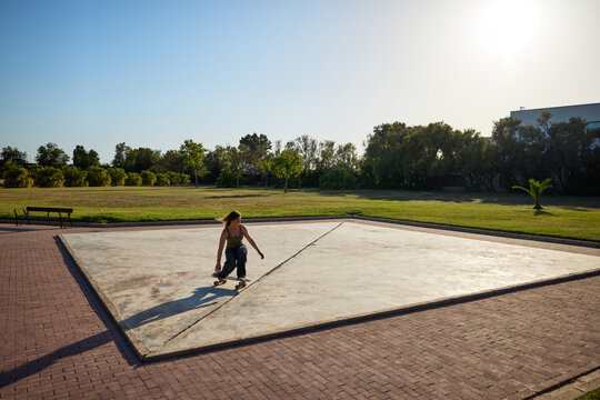 Surfskater performs tricks on empty concrete pad in park
