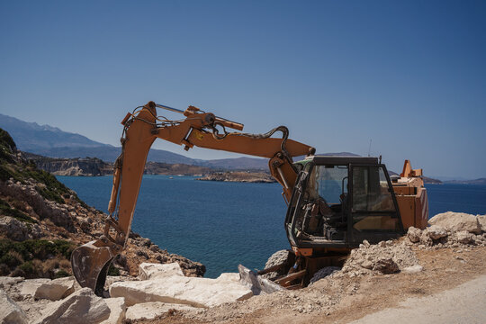 excavator on a cliff with sea at the background