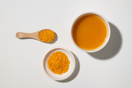 Bright yellow turmeric powder and liquid in bowls with a wooden spoon