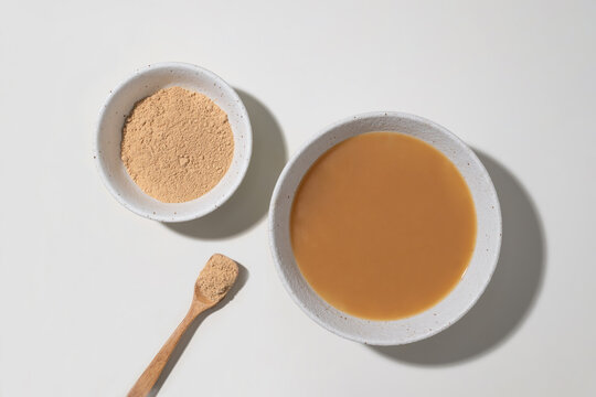 Two bowls of maca powder and liquid maca drink with a wooden spoon