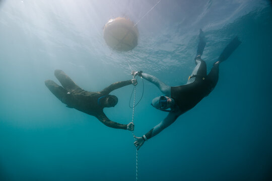 two freedivers meeting underwater beside a buoy line