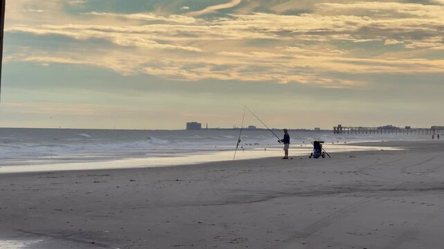 isherman on a deserted beach fishing in the surf with  a dramatic cloudy sky.