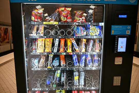 Vending machine filled with various packaged snacks, candy bars, and refreshing drinks. Automated dispensing machine stocked with an assortment of chips, sweets, and beverages.