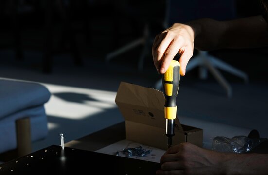 Hands using a screwdriver to assemble a flat-pack item in a home setting, showcasing the DIY approach during economic recession periods for affordable solutions