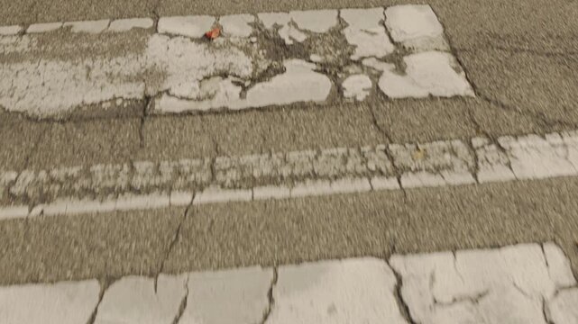 A low-angle view highlights the textural details of the weathered road signs and the damaged road infrastructure on a public urban road strewn with autumn leaves