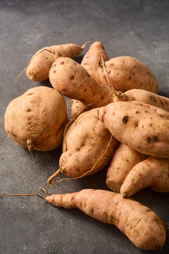 pile of raw sweet potatoes on dark gray textured surface, unpeeled root vegetables in close-up view with copy space, healthy organic farming harvest