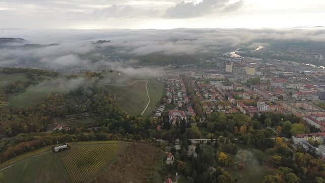 Aerial drone footage of Maribor, Slovenia, surrounded by autumn-colored hills and vineyards as thick fog drifts across the city and the Drava Valley.