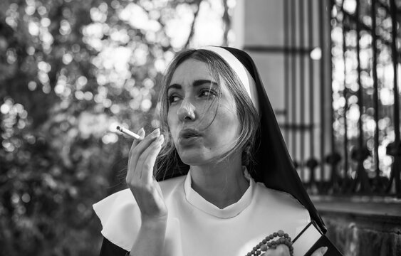 Thoughtful woman wearing a traditional nun inspired habit and holding a cigarette. Dramatic conceptual portrait exploring faith, personal identity, inner conflict, rebellion and the contrast 